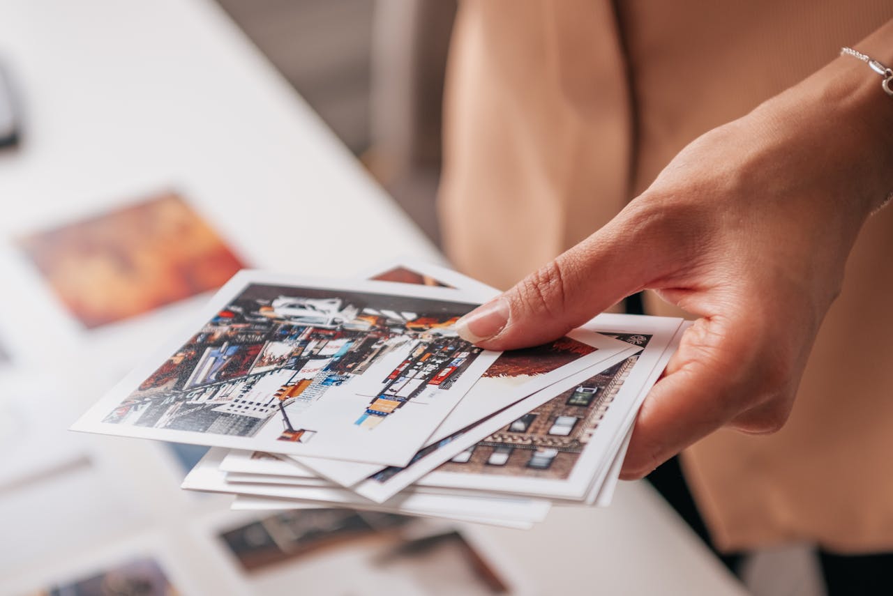 heros-img A hand holding printed photographs featuring urban cityscapes on a white table.